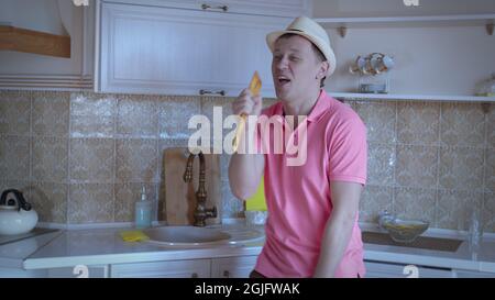 Man in a pink T-shirt and a hat is dancing and singing in the kitchen, good mood, positive emotions Stock Photo