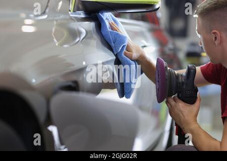 Man repairman wiping car with microfiber cloth and holding polishing machine in his hand closeup Stock Photo