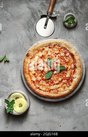 Tasty pizza with  chicken, mozzarella, pineapple on marble round tray. Garnished on grey stone backdrop with pizza ingredients Stock Photo