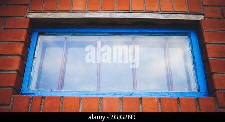 Low window with old blue frame and iron grating in a orange brick building. Stock Photo
