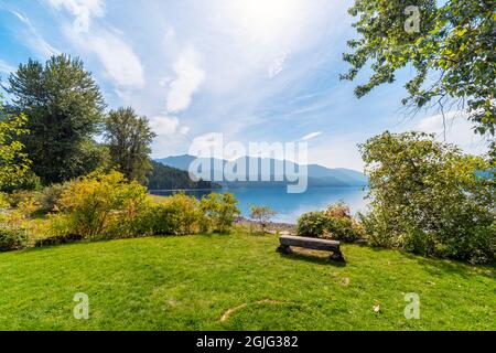 A small bench sits in a park at the Kohan Reflection Gardens overlooking Slocan Lake in the town of New Denver, BC, Canada. Stock Photo