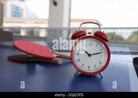 Red alarm clock standing on tennis table near rackets closeup Stock Photo