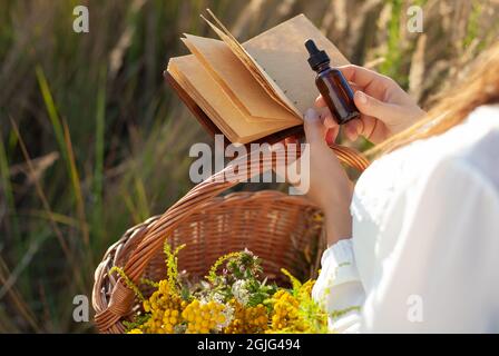 Herb extract in a dropper, copy-space for text. Woman holding a medical bottle and a blank notebook in her hand. Natural Remedy, conceptul - MOCK-UP. Stock Photo