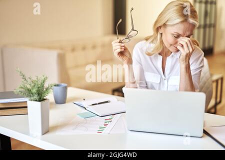 Tired mature businesswoman took off her glasses, massaging nose bridge, suffering from dry eyes syndrome Stock Photo