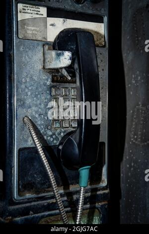 Old dirty vintage payphone on city street covered in car exhaust and debris Stock Photo