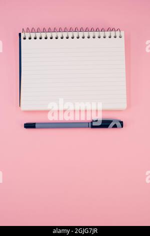 Vertical shot of an open notebook with a pen on a pink surface Stock Photo