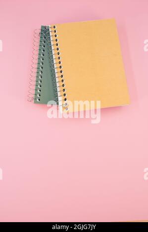 Vertical shot of yellow and green notebooks on a pink surface Stock Photo