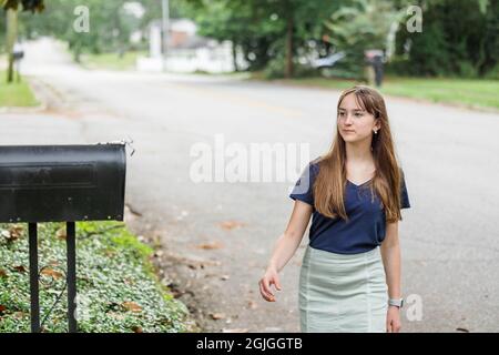 A teen brunette girl with long hair checking the mailbox for letters and packages. Stock Photo