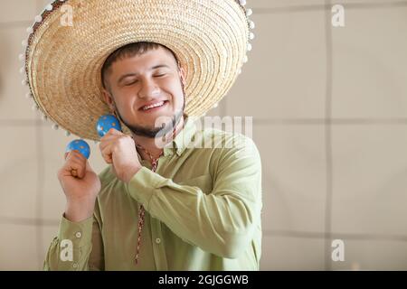 Young Mexican man in sombrero hat and with maracas at home Stock Photo