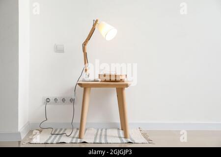 Glowing lamp and books on table near light wall Stock Photo