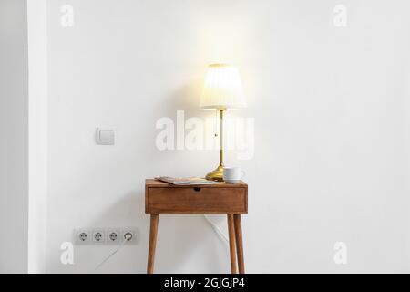 Glowing lamp and magazine on table near light wall Stock Photo