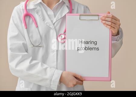 Female doctor holding clipboard with text HEARING PROBLEMS on color background Stock Photo