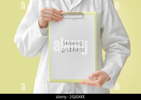Female doctor holding clipboard with text HEARING PROBLEMS on color background Stock Photo