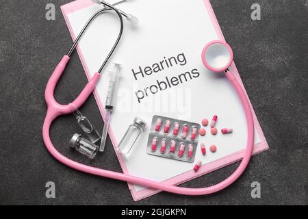 Clipboard with text HEARING PROBLEMS, stethoscope and pills on dark background Stock Photo