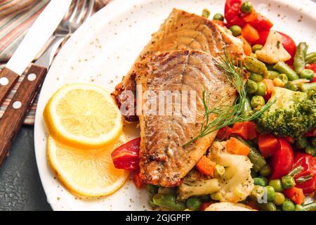 Plate with tasty baked cod fillet and vegetables on dark background, closeup Stock Photo