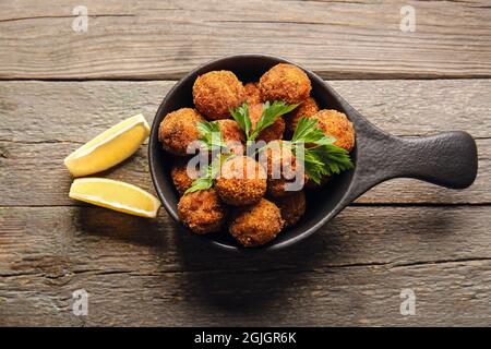Frying pan with tasty cod cutlets and lemon on wooden background Stock Photo