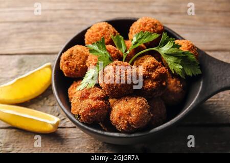 Frying pan with tasty cod cutlets and lemon on wooden background, closeup Stock Photo