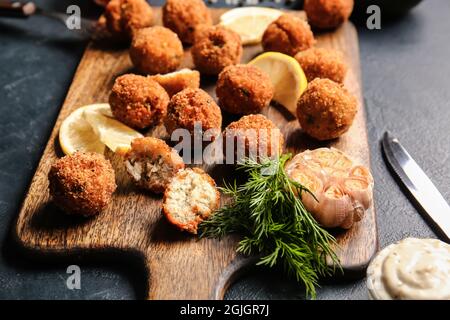 Board with tasty cod cutlets and sauce on dark background, closeup Stock Photo
