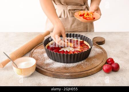 Woman cooking plum pie at table Stock Photo