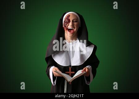 Crazy woman dressed for Halloween as nun with Bible on dark color background Stock Photo