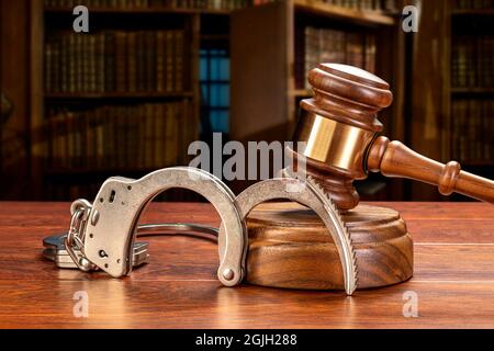 A pair of handcuffs rests against a judge's gavel and block in a judge's law chamber.  For inferences regarding public safety, crime, law and punishme Stock Photo