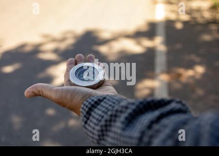 Male traveler holding a magnetic compass on asphalt road, orientation and finding your way. Stock Photo