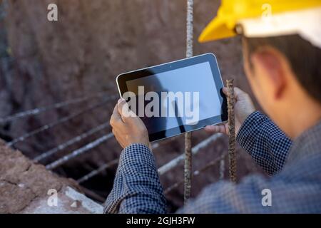 architect or civil engineer with hardhat on construction site checking schedule on tablet computer Stock Photo
