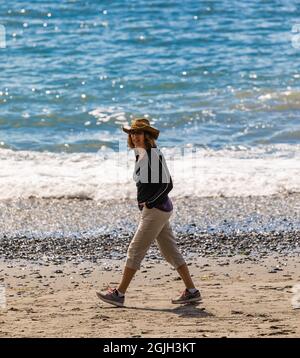 Active woman wearing a hat walks along the shore of a beach at Vancouver Island BC, Canada-August 9,2021. Street view, travel photo, selective focus, Stock Photo