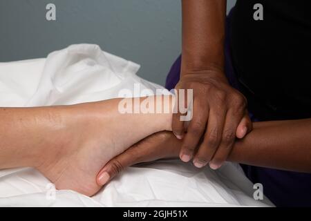 Black female massage therapist massages the foot of a white female client Stock Photo