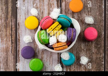 Delicious macaroons, a famous multicoloured French dessert in a bowl and scattered on the table. Selective focus. Blurred background Stock Photo