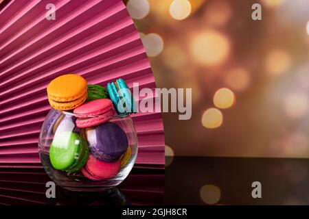 Delicious macaroons, a famous multicoloured French dessert in a clear crystal glass. Selective focus. Blurred background Stock Photo