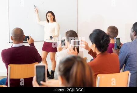 Students shooting lesson on smartphones , teacher standing at blackboard Stock Photo