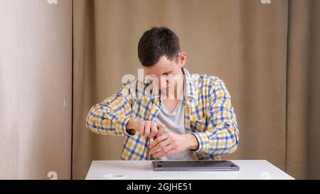 Young man disassembles a laptop with a screwdriver while sitting at table Stock Photo