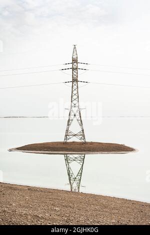 high voltage transmission power tower or electricity pylon installed on a man-made artificial island in the Dead Sea in Israel on a cloudy day Stock Photo