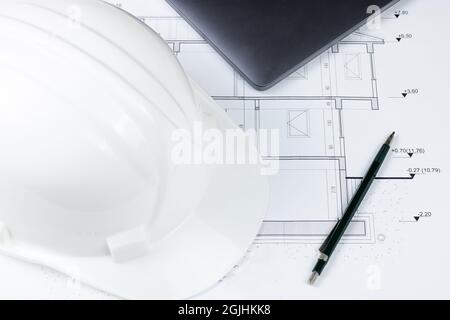 A pen, a white safety helmet and a laptop on the architectural plan Stock Photo