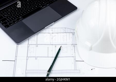 A pen, a white safety helmet and a laptop on the architectural plan Stock Photo