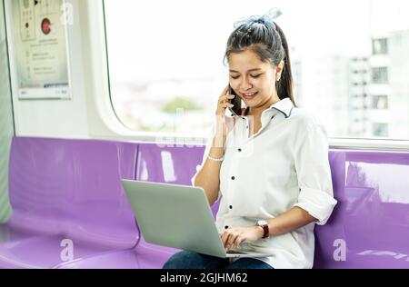 Asian businesswoman talking on cellphone and working on laptop while traveling by sky train Stock Photo