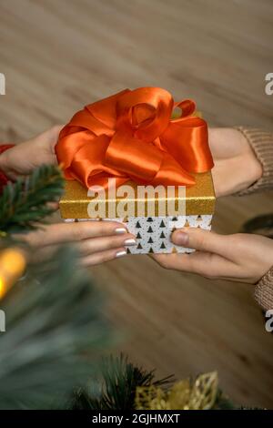 Hands of man giving a Christmas gift with red bow to womans hands near the christmas tree. Stock Photo
