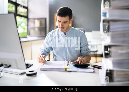 Young Businessman Working At Office With Stack Of Folders On Desk Stock Photo