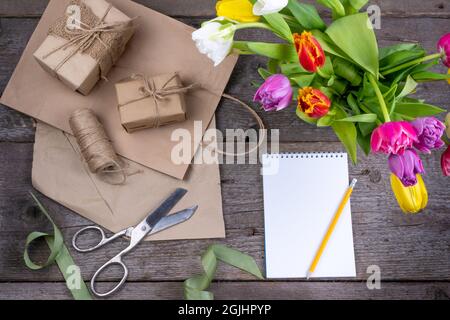 List of purchases and gifts. Notebook with place for text. Gift wrapping for the holiday on wooden table. top view. Bouquet of tulips flatlay Stock Photo