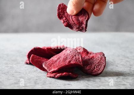 Take a piece vegetable beetroot chips on a gray background. Vegan snack. Close up. Stock Photo