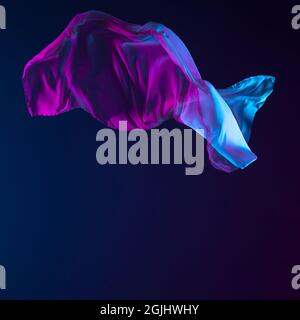 Beautiful and elegant flowing piece of blue silk fabric isolated over dark blue background. Delicate cloth Stock Photo