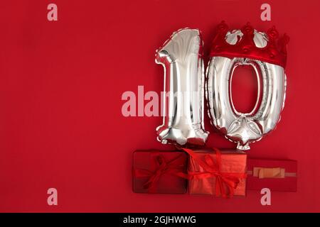 Foil silver air balloons showing number 10 ten placed on red background with wrapped presents for concept of birthday anniversary Stock Photo