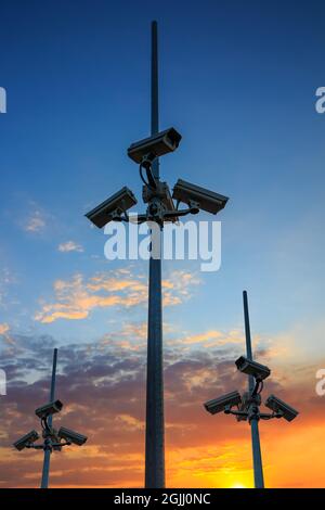 Many security cameras watching all around. CCTV equipment on dramatic sunset background Stock Photo