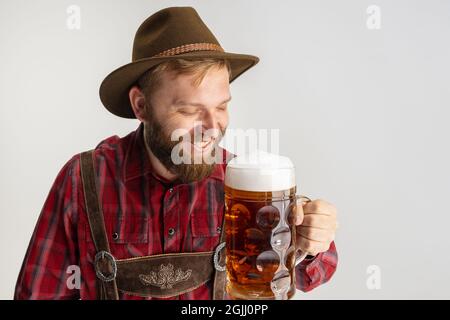 Half-length portrait of bearded man in hat and traditional Bavarian costume holding huge mug, glass of light frothy beer isolated over white Stock Photo