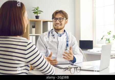 Young male doctor tells and explains to female patient her diagnosis during consultation at clinic. Stock Photo