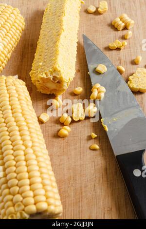 Fresh corn being chopped with a knife on a bamboo wooden board. Stock Photo