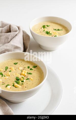 Two bowls of homemade corn chowder topped with fresh parsley and corn kernels. Stock Photo