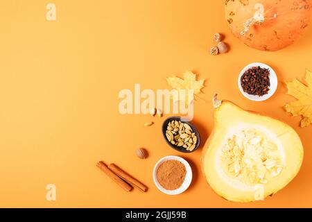 Pumpkin spices next to hokkaido pumpkins and autumn leaves on orange background with copy space, flat lay. Stock Photo