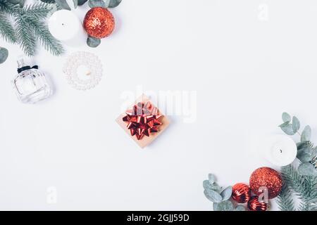 Christmas composition small gift box among fir branches, red ornaments and candles on white background, flat lay. Stock Photo